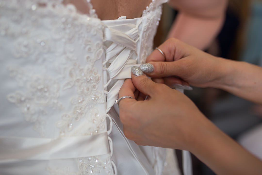 bridesmaid lacing up bride's dress