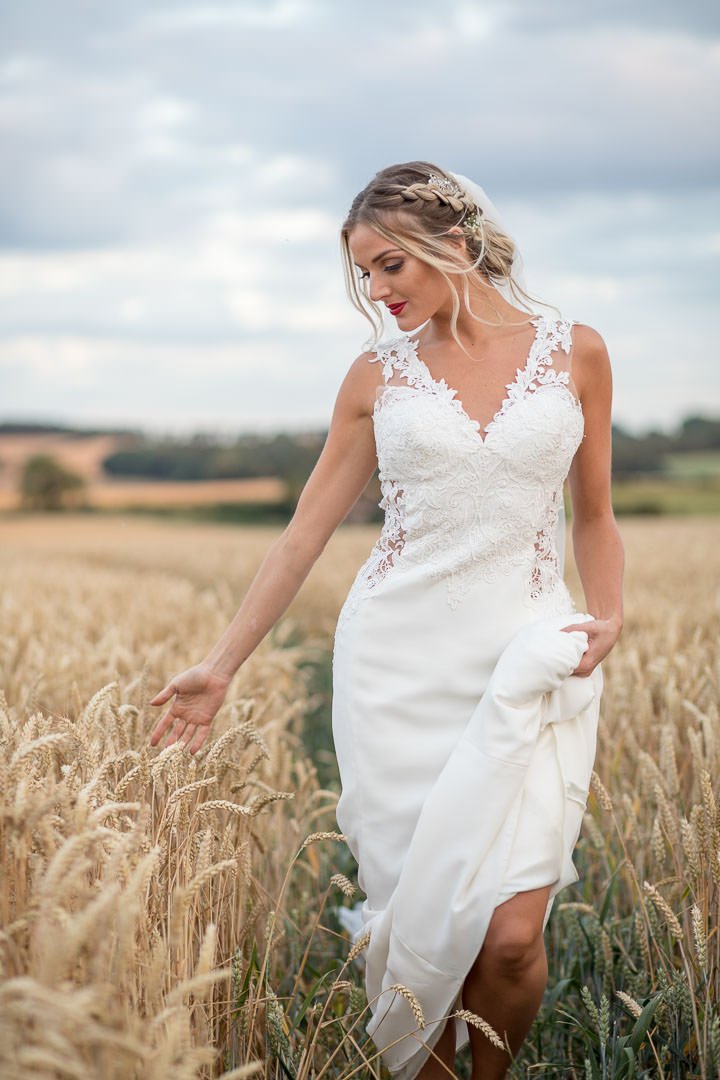 Boho bride walks in Hampshire cornfield with hand trailing in the corn