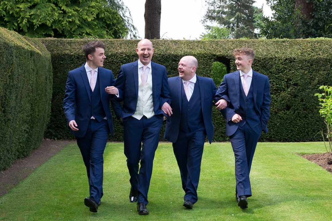Groom and groomsmen walk arm in arm on the  lawn at Barnett Hill Hotel