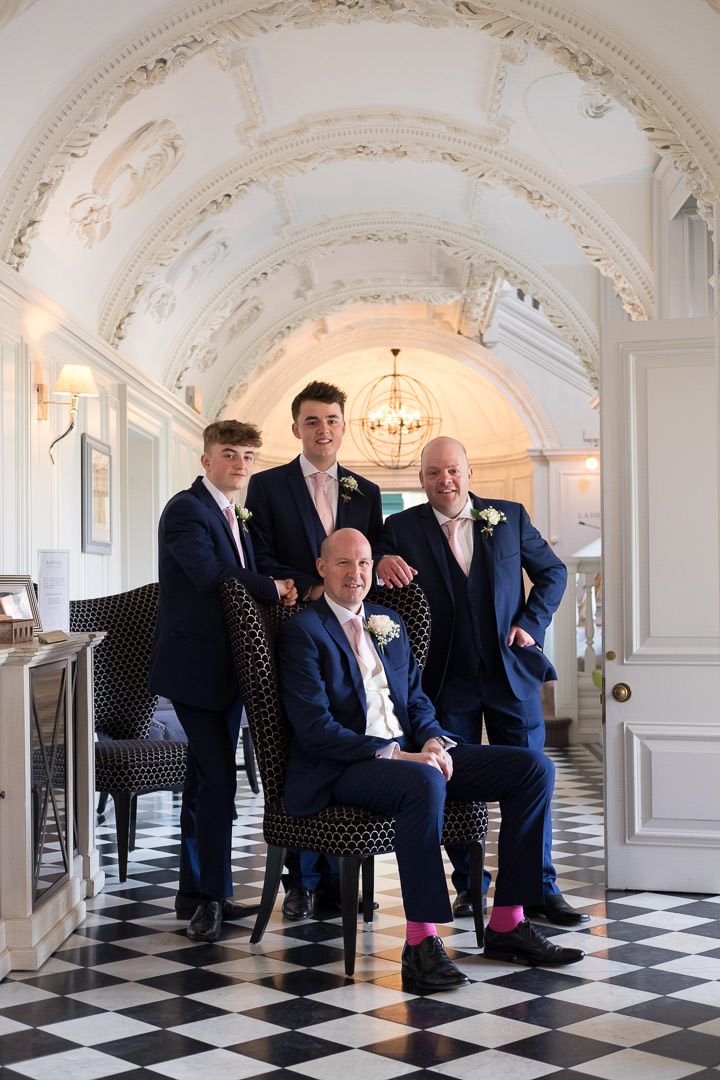 groom sits and his groomsmen stand around him in the downstairs hall at Barnett Hill