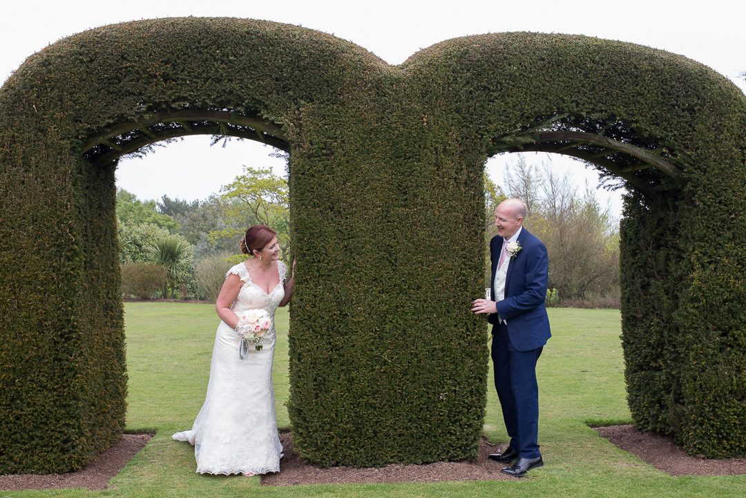 The bride and groom peering at each other under the topiary arches 