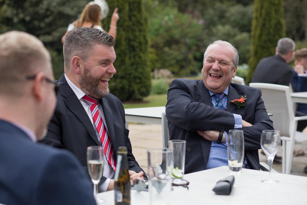 wedding guests laugh together as they sit on the terrace during the drinks reception at Barnett Hill Hotel