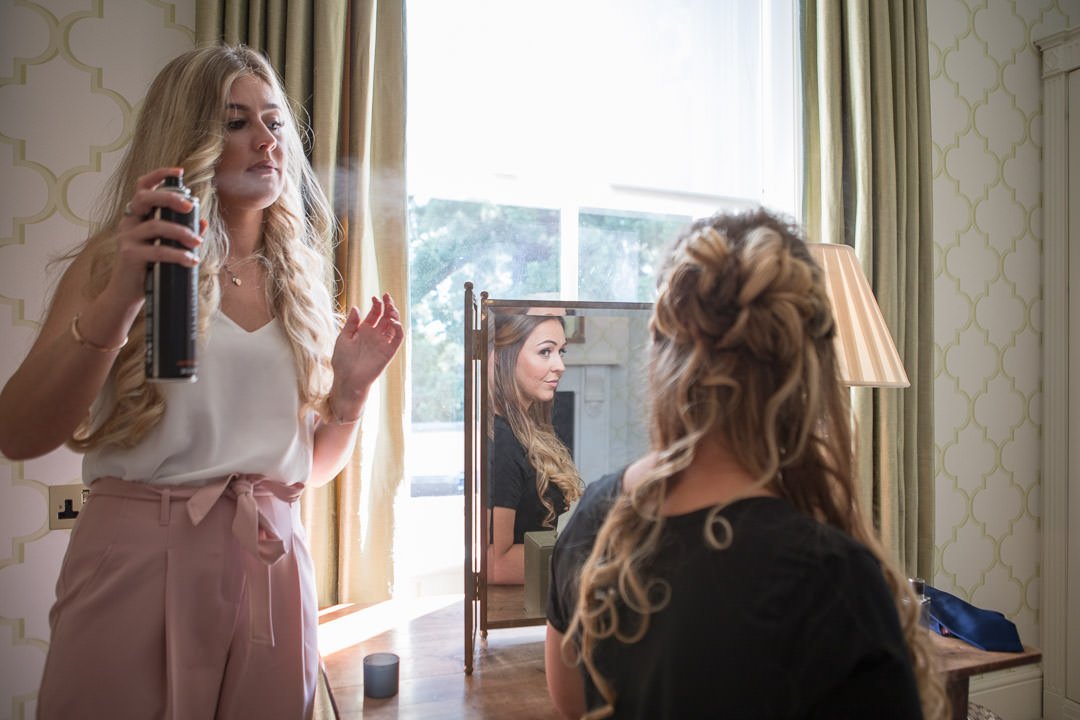 The bride looks in the mirror as she is having her hair done during bridal preparation at the Vineyard in Stockcross, wedding venue near Newbury in Berkshire