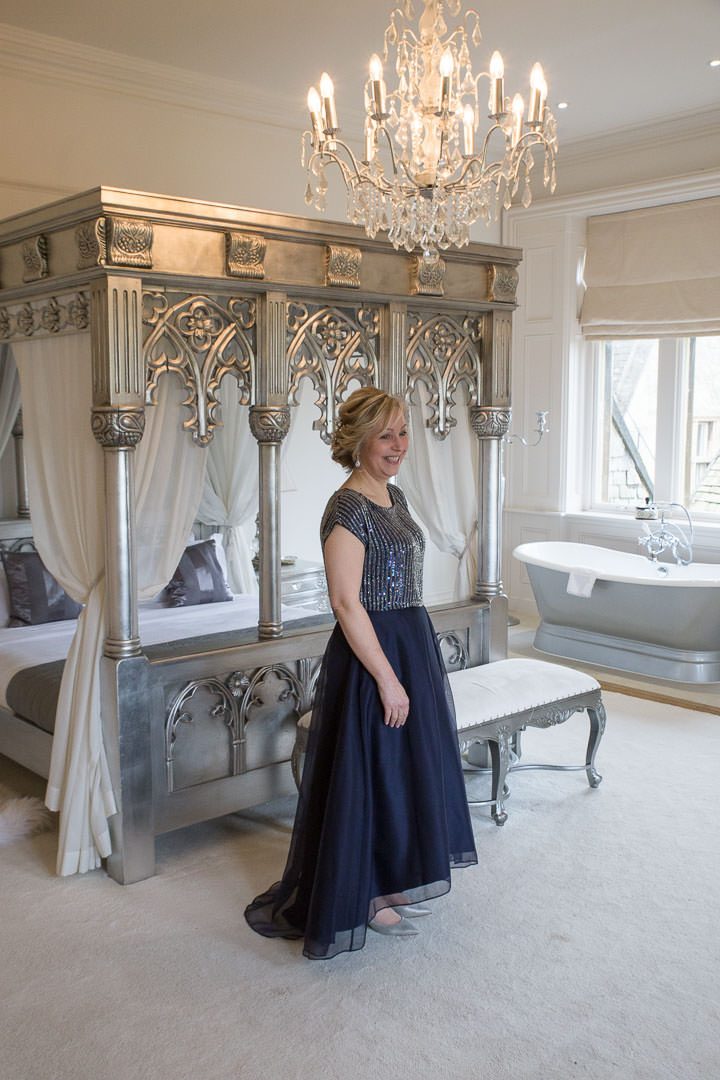 the bride in a navy sequinned top and satin mid length skirt stands by a silver four poster bed