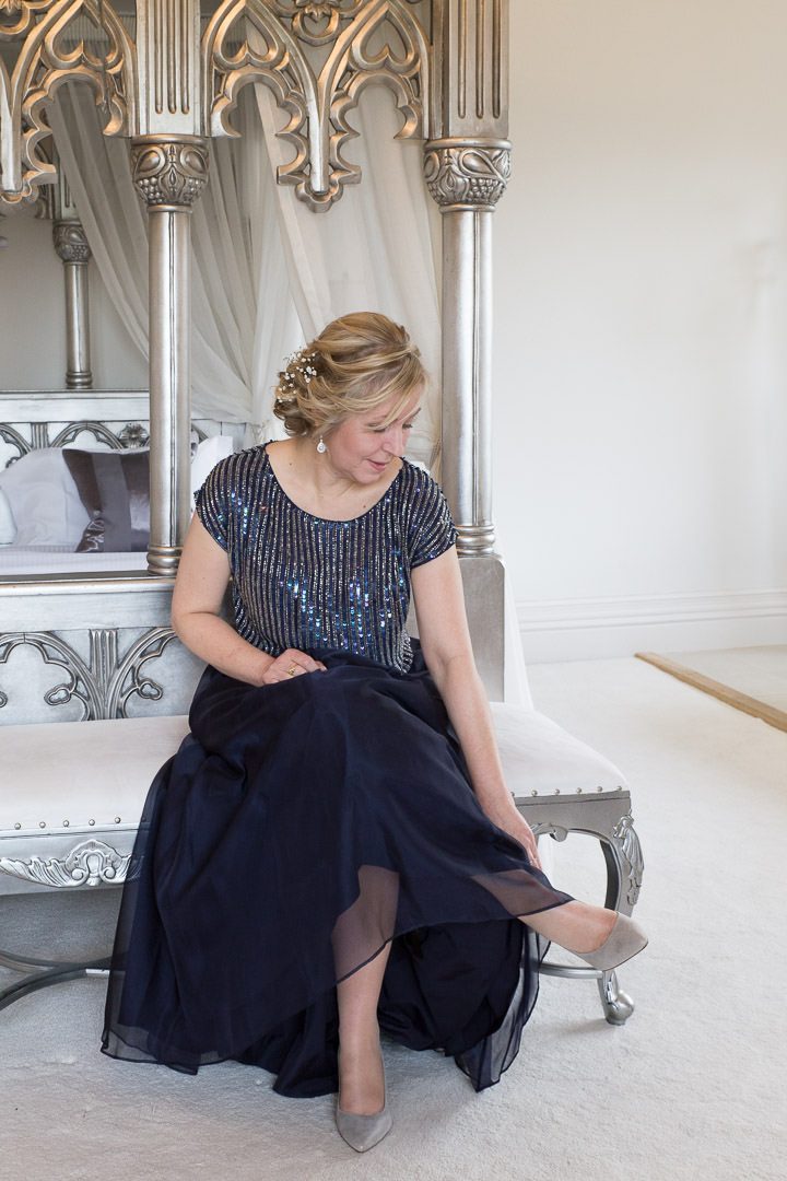 the bride in navy sequinned top and satin skirt sits on a bench as she puts on her shoe