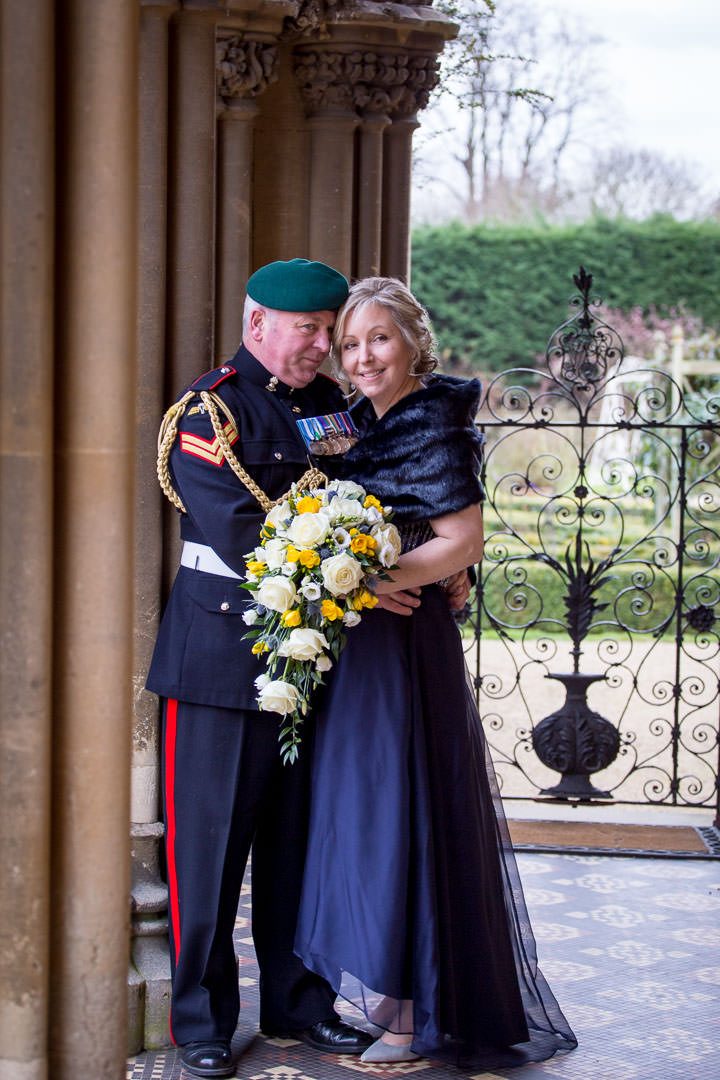 the bride, dressed in blue, and her military groom embrace in front of a wrought iron gate