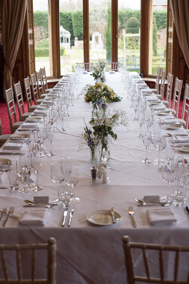 a long table set up for the wedding breakfast, with little jars of white flowers
