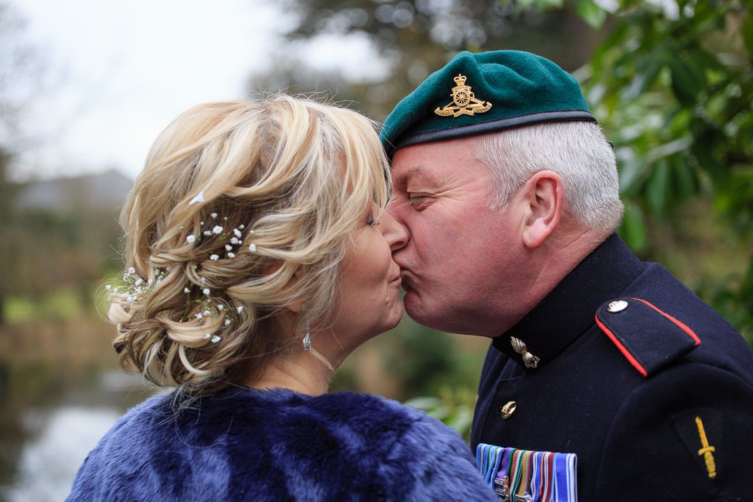 closeup of the bride and groom kissing, he wears a green military beret