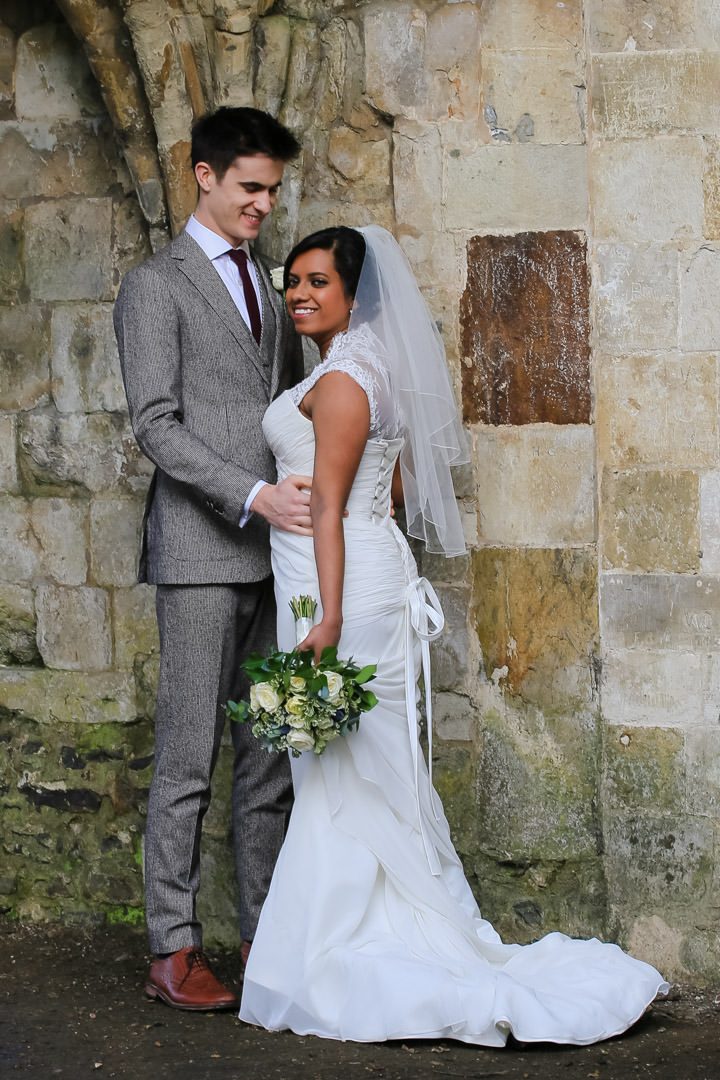 bride and groom pose together in front of an old stone wall