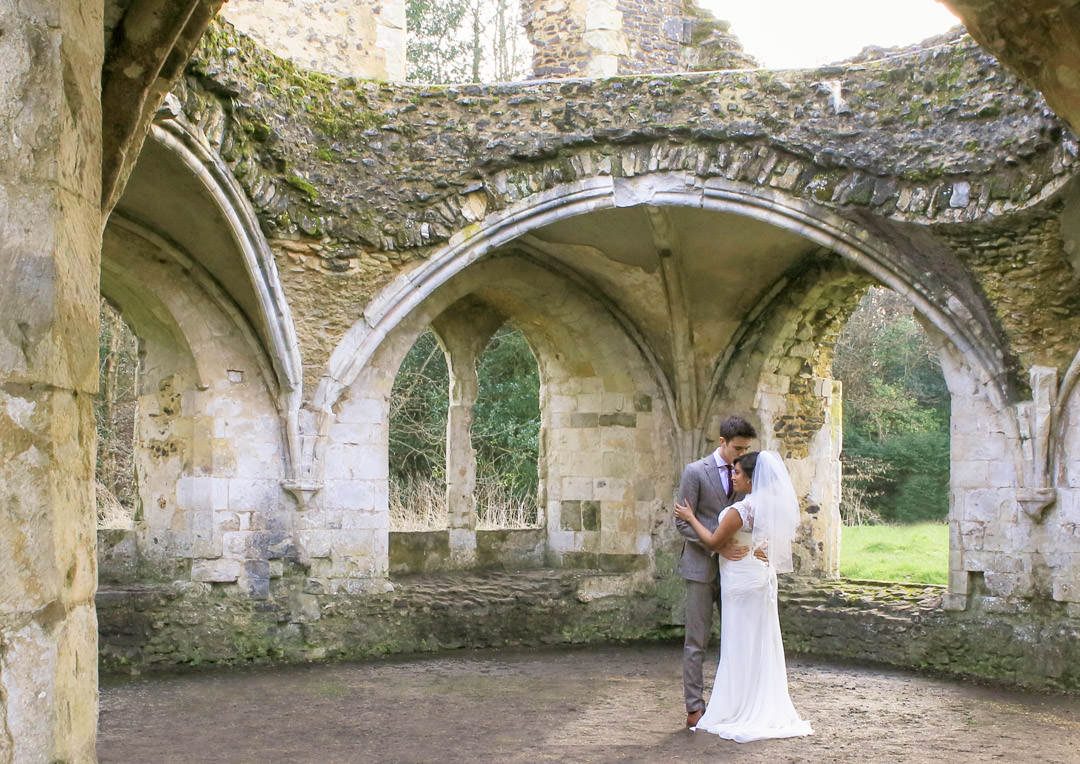 Groom kisses the bride's forehead as they embrace in the ruins of the Abbey