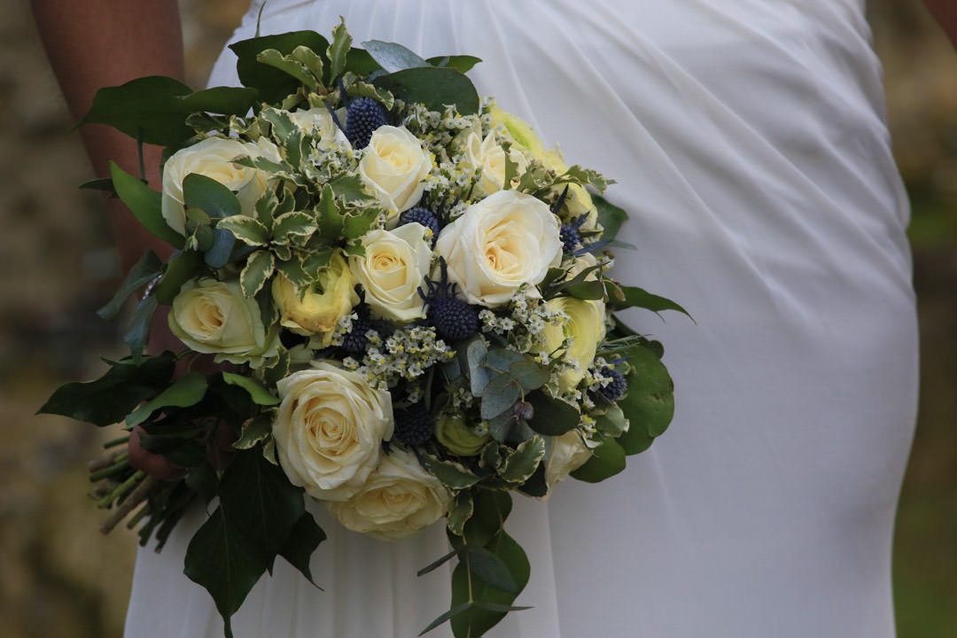 Detail shot of a bridal bouquet of cream and yellow roses, with variegated euonymus and blue sea holly