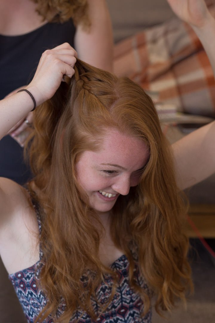Redheaded bride plaits her hair as she gets ready for her wedding