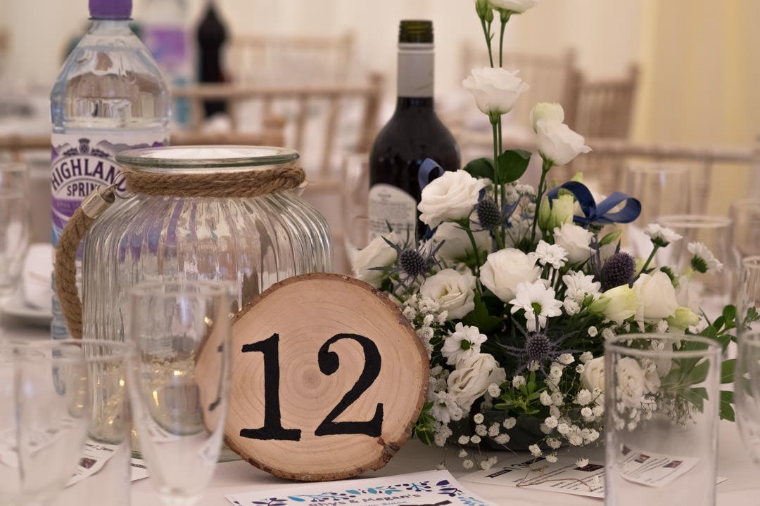 wedding breakfast table details, show table number on a sliced log, hurricane lantern and blue and white flowers