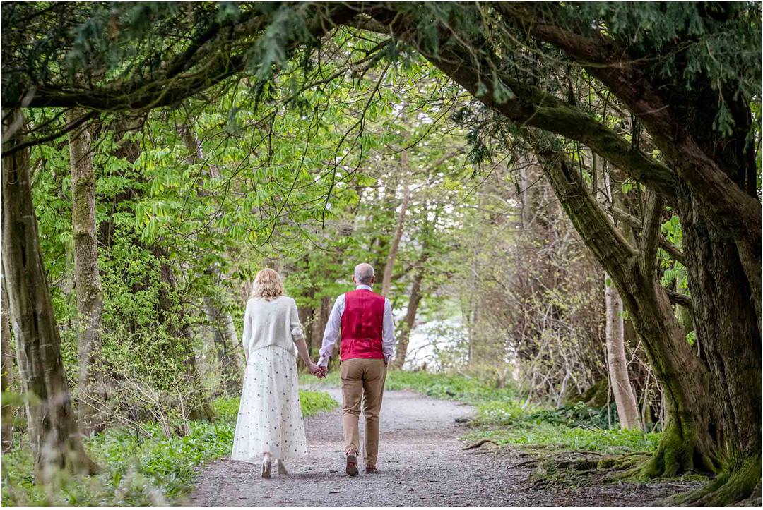 The bride and groom walk away through the archway of trees by Lake Coniston