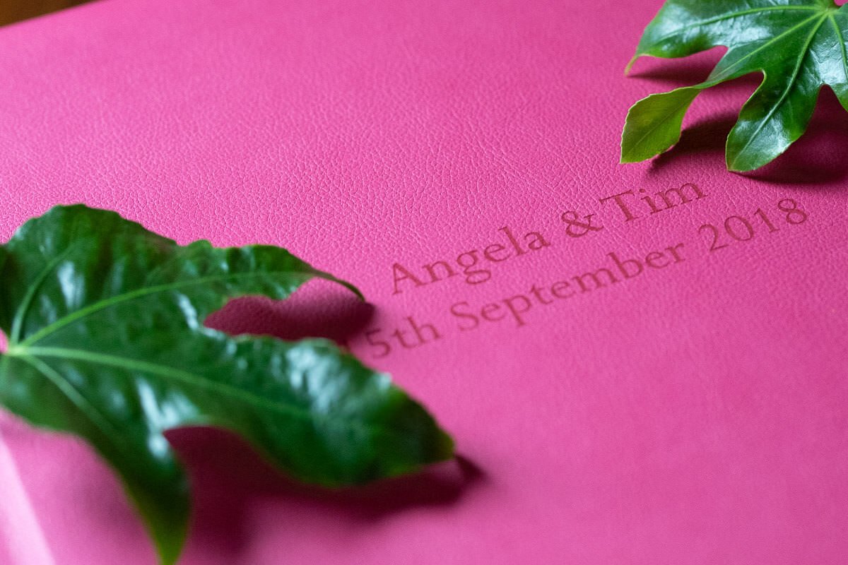 bright pink wedding album etched with couple's name and date, decorated with green glossy leaves