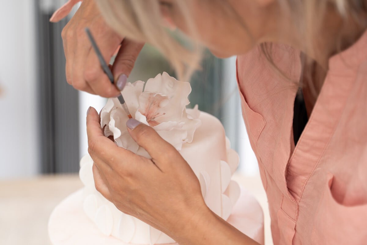close up of cake maker using a paint brush to apply the final touches to a wedding cake
