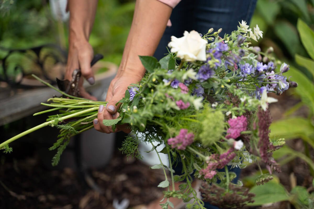 closeup of a florists hands as she cuts the stems on the bouquet that she is assembling in the garden