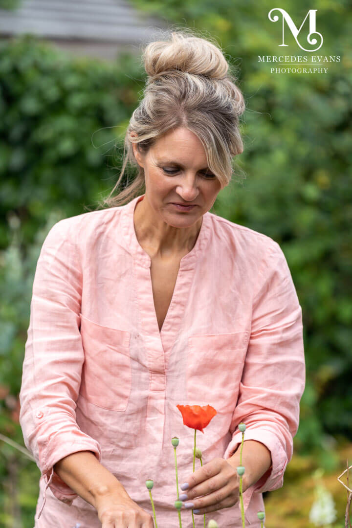 female gardener wearing a pale pink shirt cuts a red poppy
