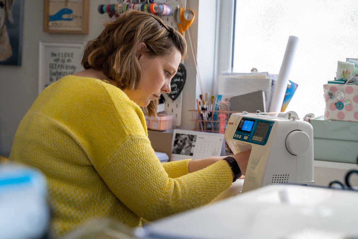 woman in a bright yellow jumper concentrates as she fiddles with her sewing machine