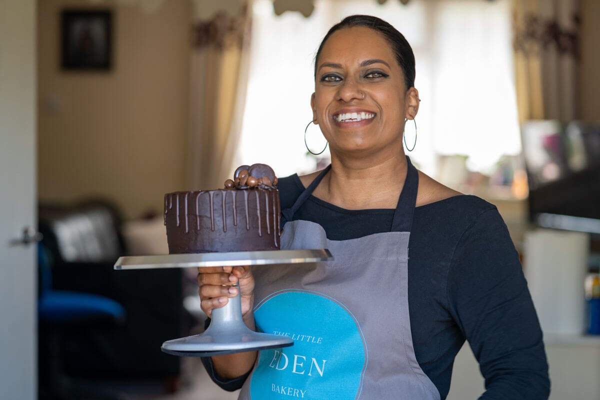 baker laughs as she holds her chocolate cake on a stand