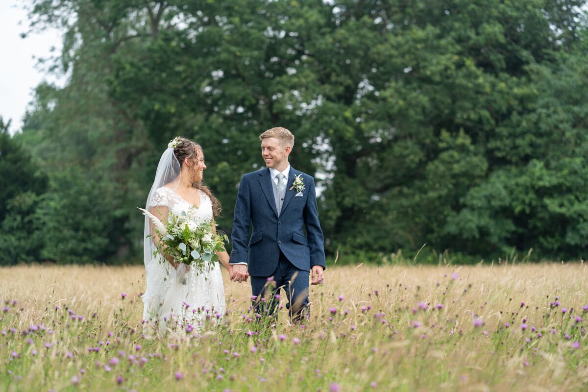 bride and groom walk hand in hand through the long grass and purple flowers