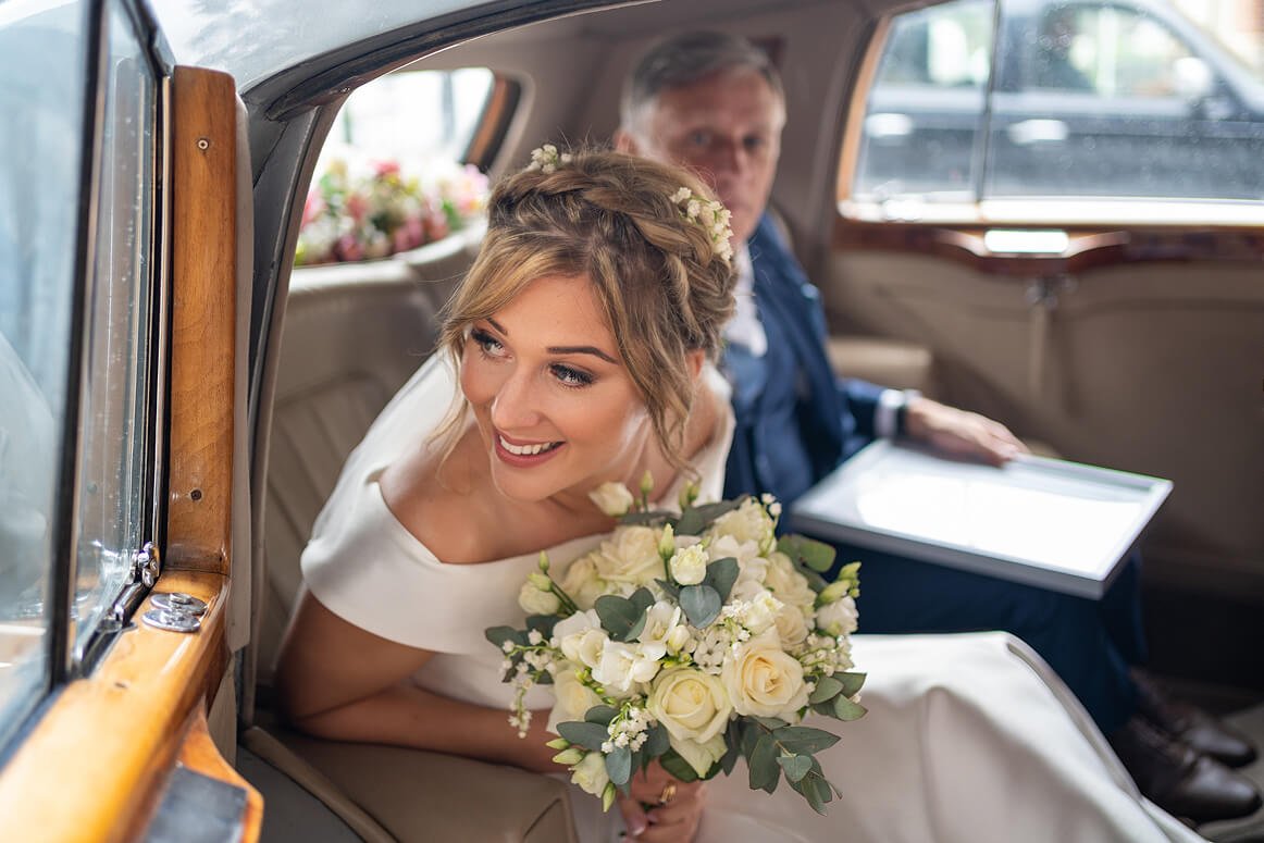 the bride leans out of the wedding car as she arrives at the church with her father