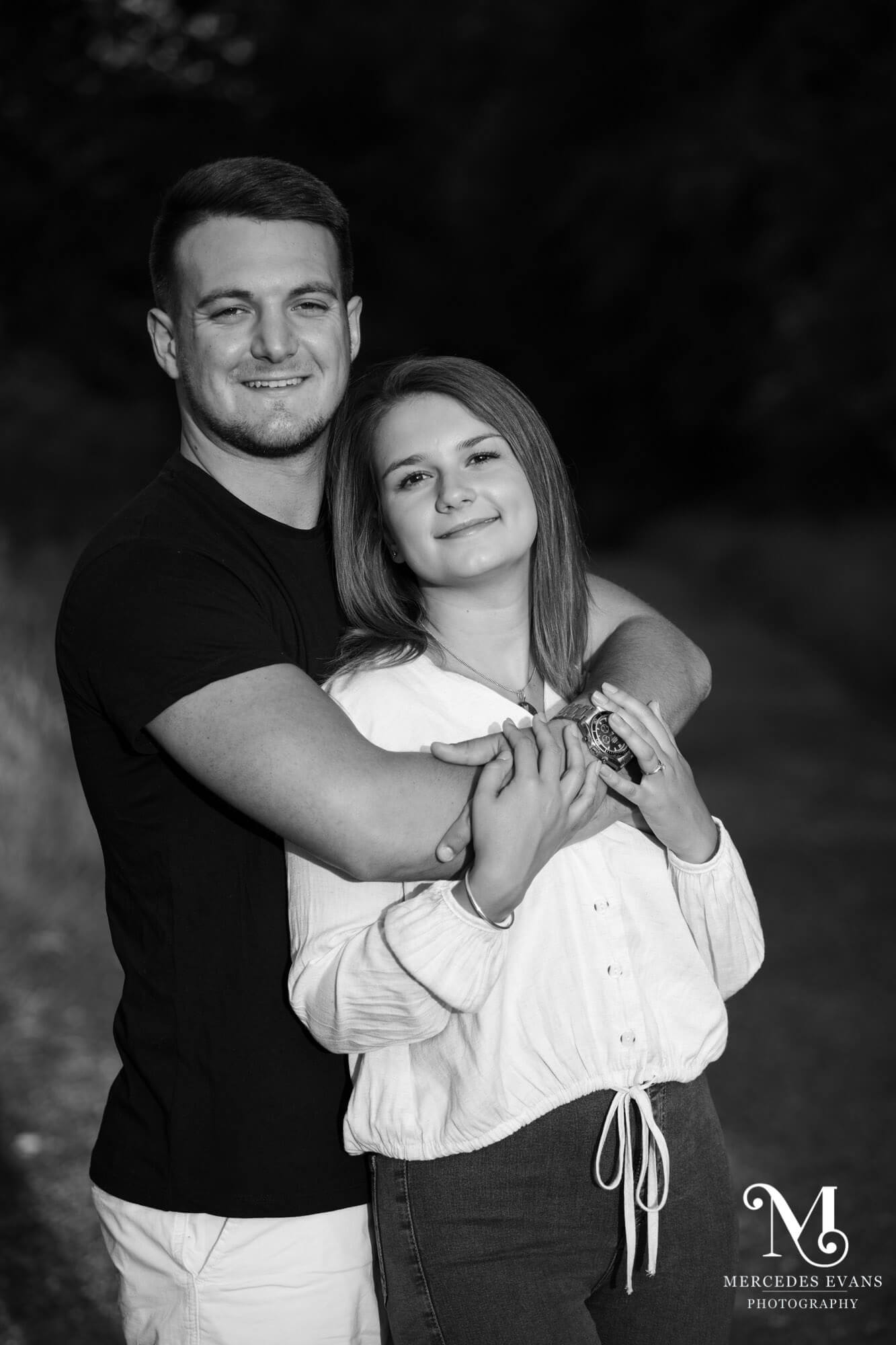 black and white image of a young man embracing a young woman, both of them are looking forward and smiling