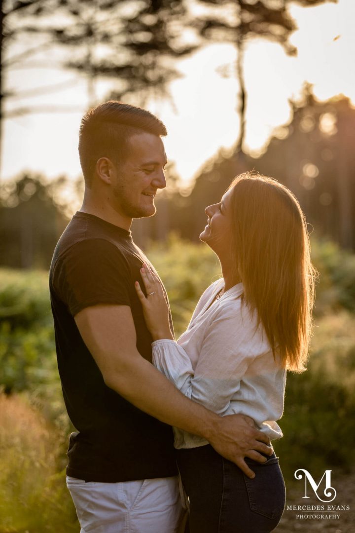 smiling young engaged couple look at each other during golden hour
