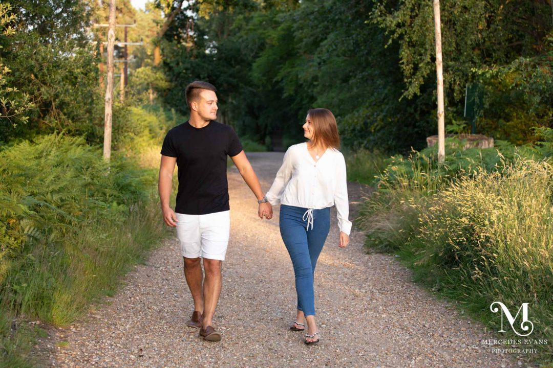 young couple walk hand in hand along a track through the woods on a sunny summer's evening
