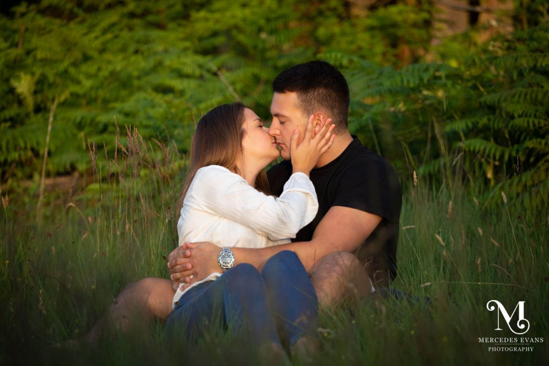 young couple sitting in long grass and kissing each other