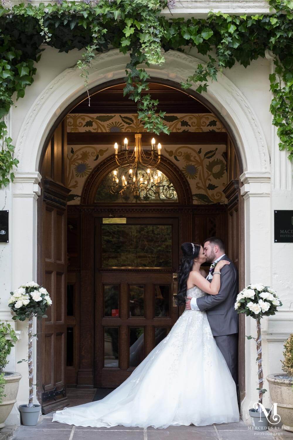 the newly weds kiss as they stand in the front doorway at Frimley Hall