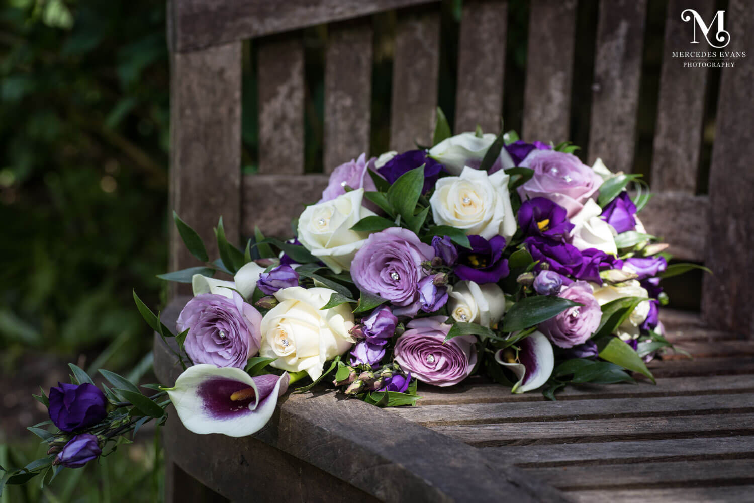 the bride's bouquet of pink and lilac roses lies on a garden bench in the sunlight