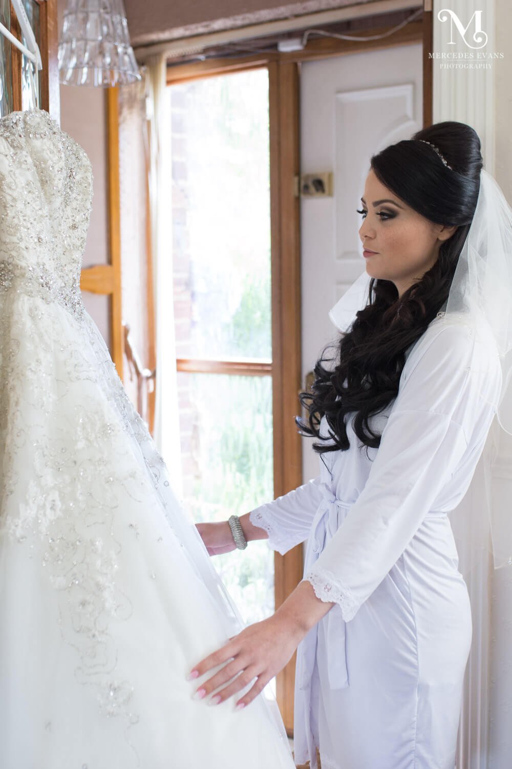 The bride admires her wedding dress as it hangs on the door