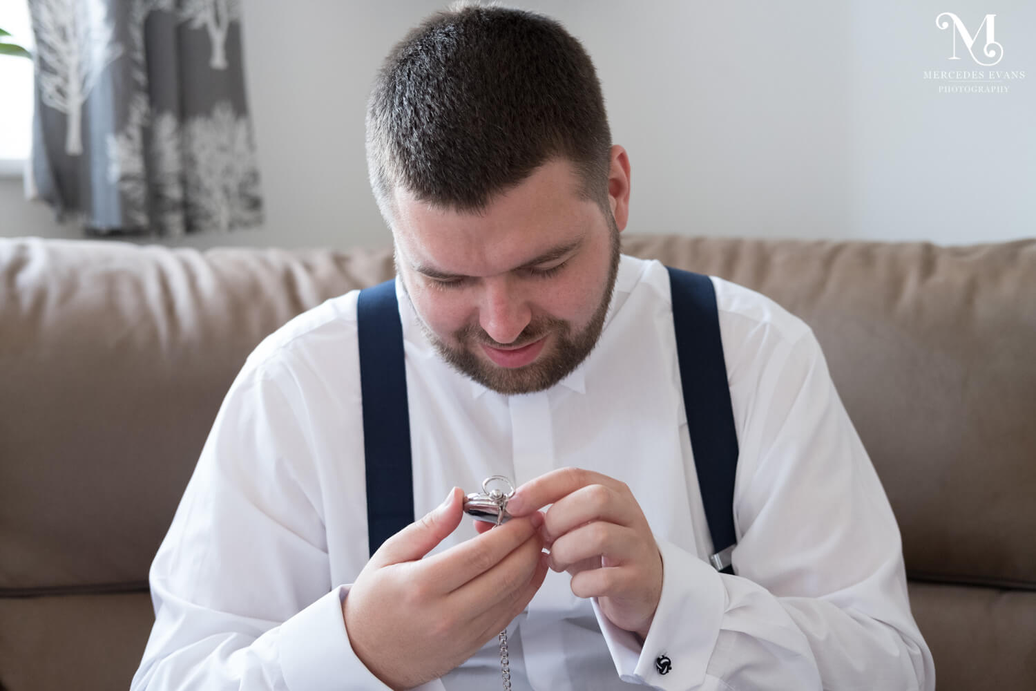 The groom looks at his pocket watch as he sits on the sofa on the morning of his wedding