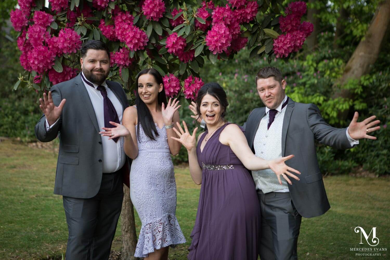 Wedding guests pose with jazz hands in front of the pink rhododendrons at Frimley Hall Hotel