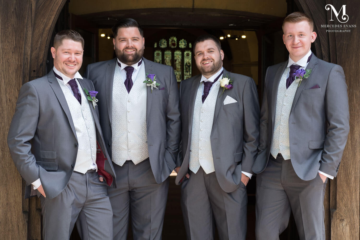 The groom and groomsmen stand in aline in the doorway of St Andrew's church in Frimley
