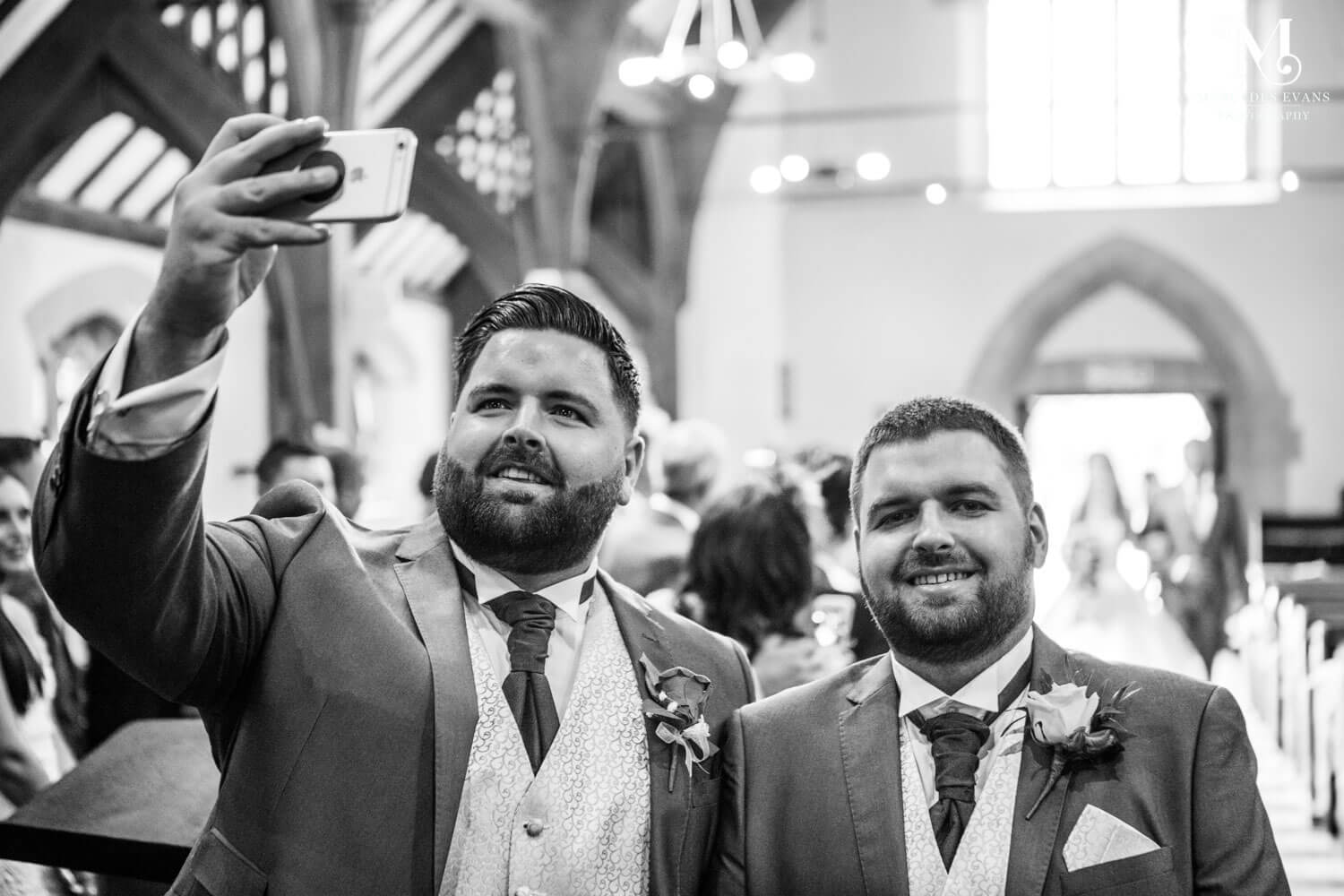 The best man and groom take a selfie as the bride walks up the aisle 