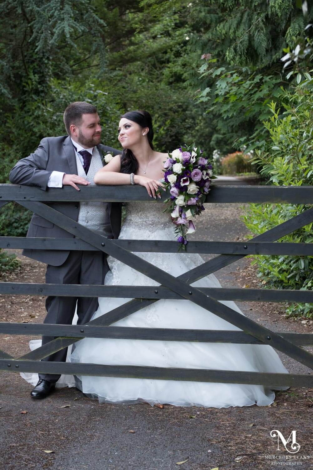 the bride and groom gaze lovingly at each other as they lean against the five bar gate at Frimley Hall