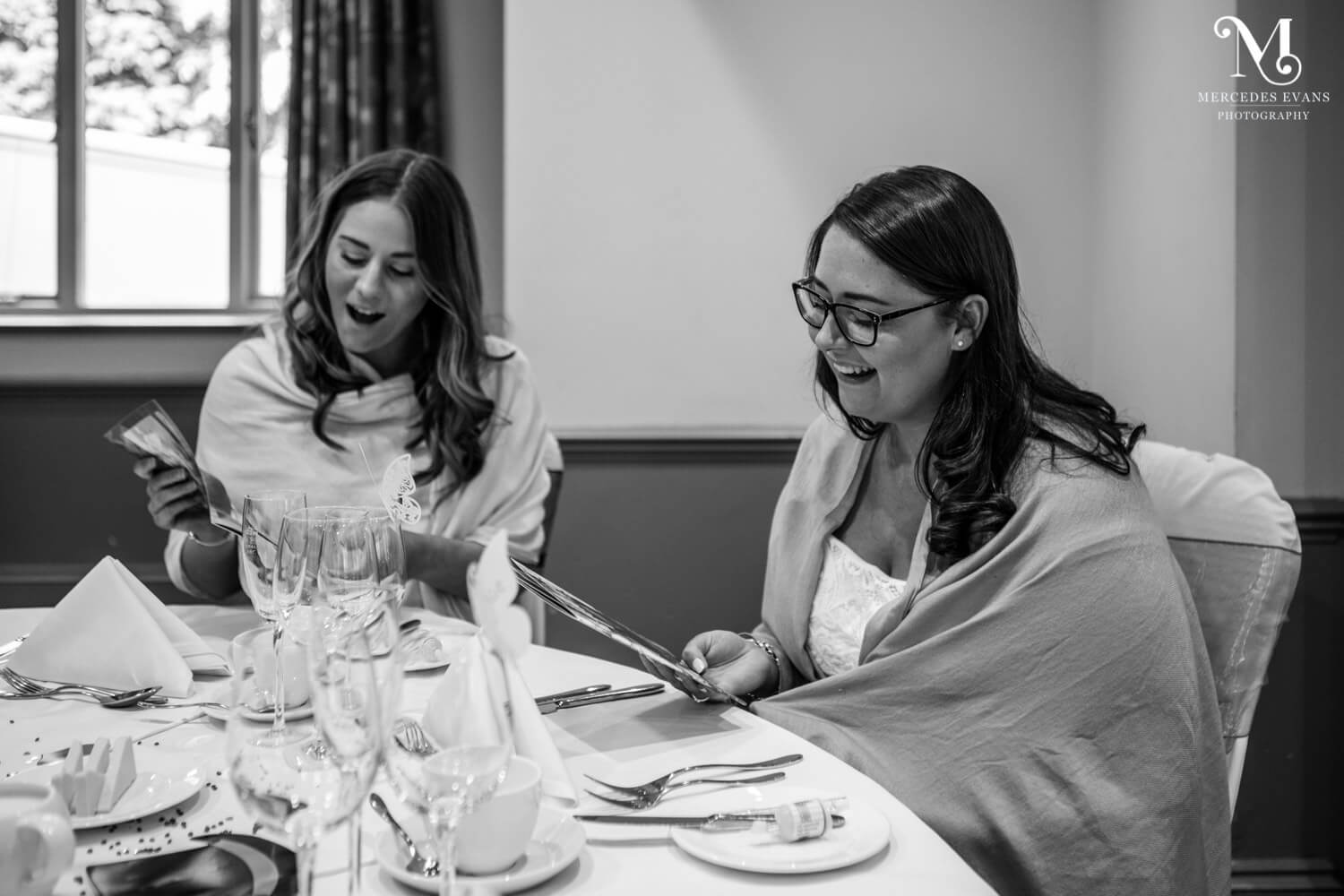 A pair of surprised female wedding guests enjoy reading the couple's personalised magazine