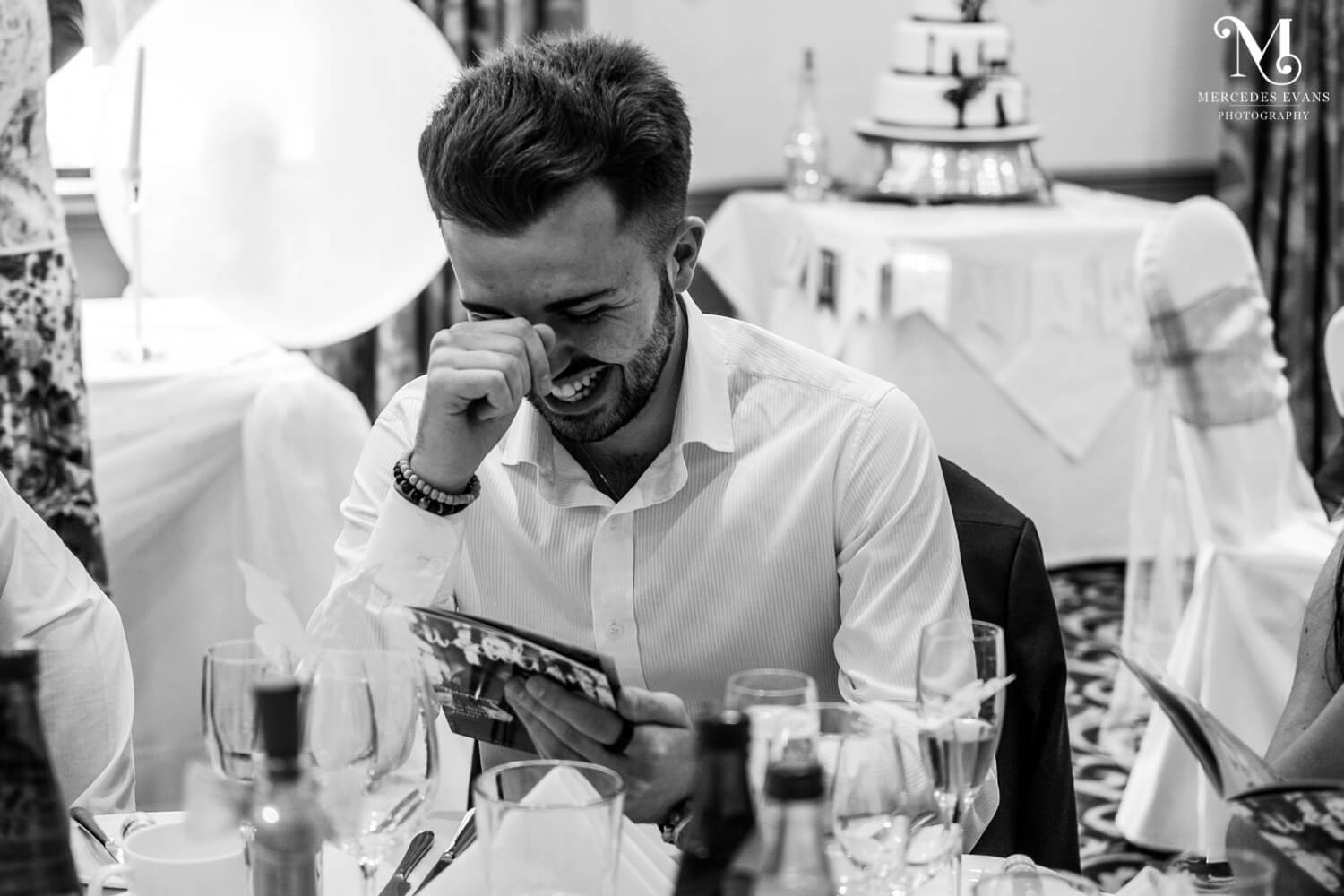 a male wedding guest laughs as he reads the couple's personalised wedding magazine