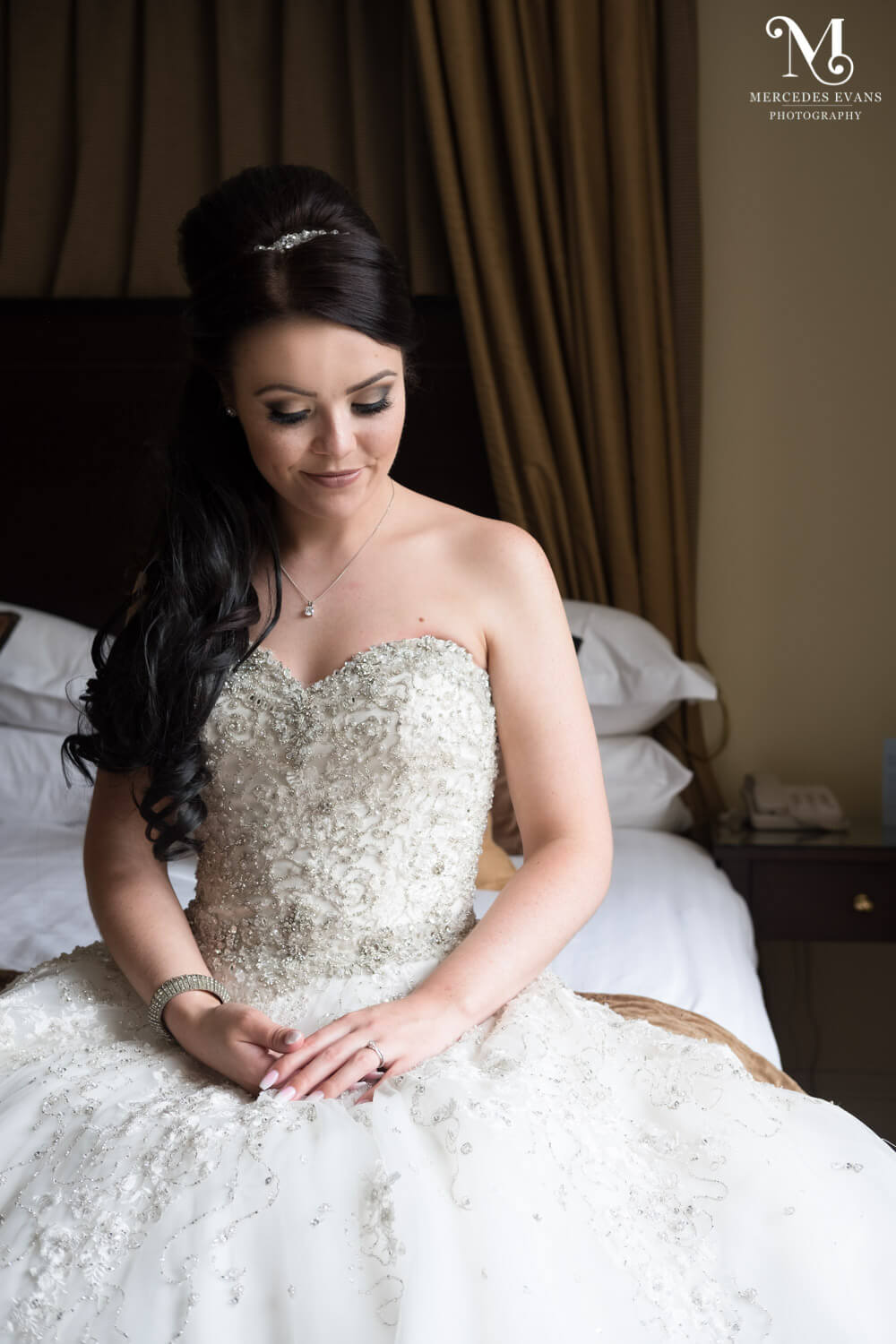 The bride sits on the bed and admires her wedding ring