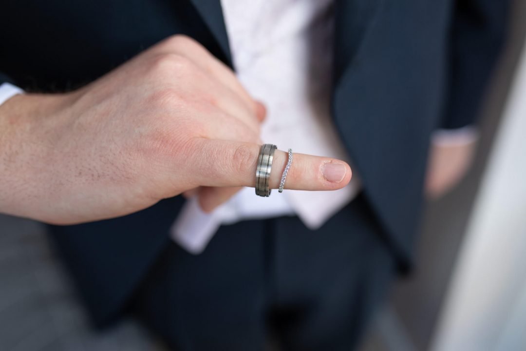 the groom wears both wedding rings on the tip of his little finger