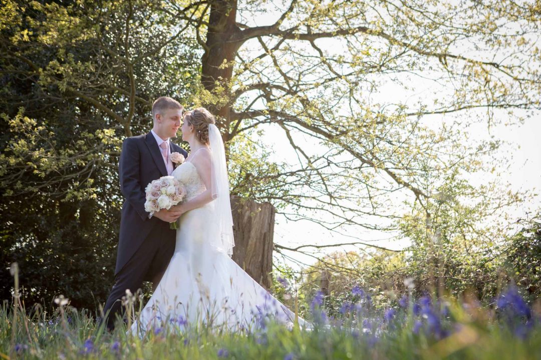 the wedding couple look lovingly at each other as they stand together in the bluebells