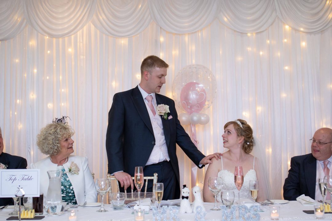 the groom reassuringly touches his wife's shoulder during his speech