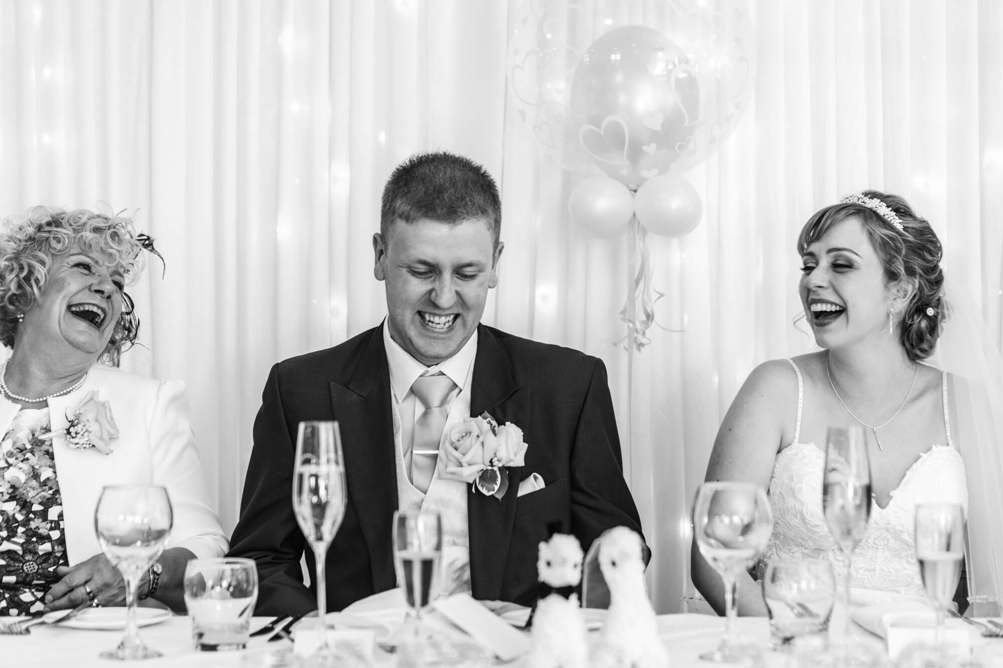 the bride and groom share a joke with his mother as they sit at table