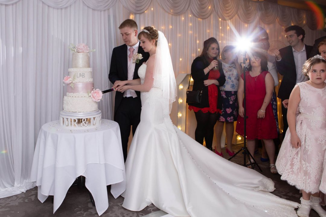 surrounded by guests, the bride and groom cut the four tiered wedding cake