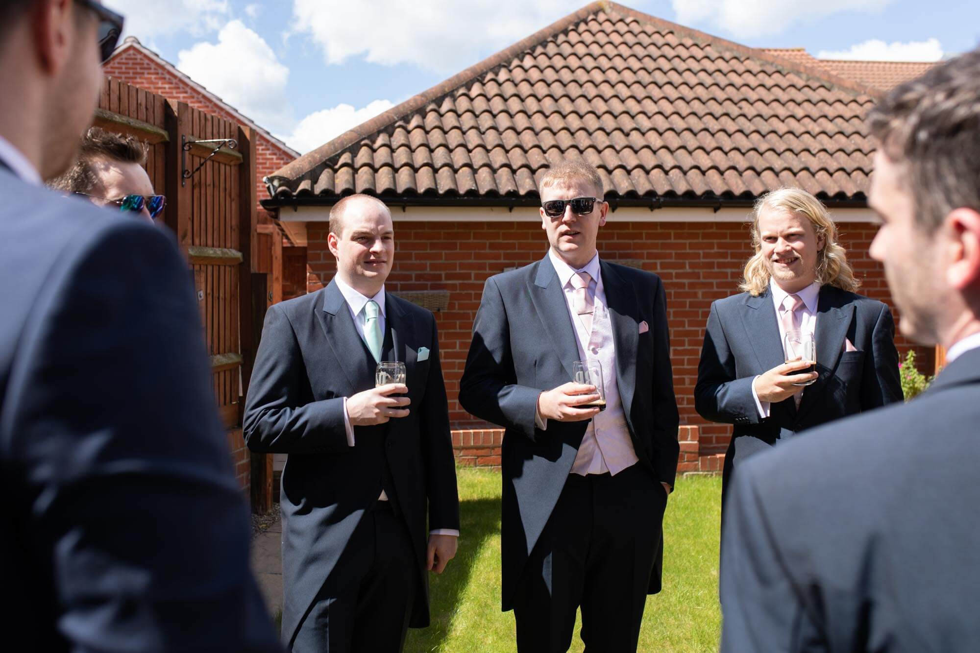 The groom and groomsmen enjoy a beer in the sunny garden before going to the wedding ceremony