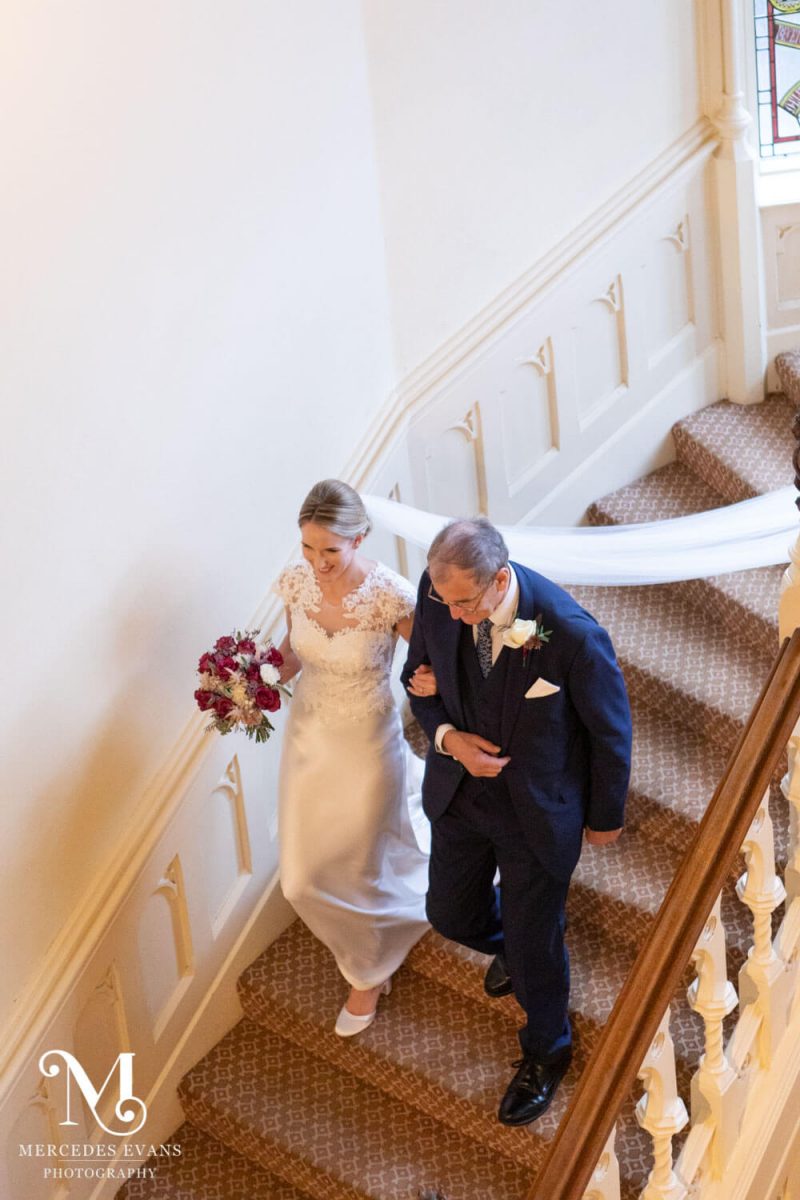 The father of the bride walks his daughter down the stairs at the Elvetham Hotel
