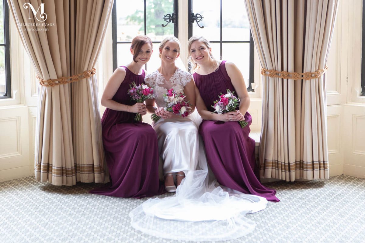 The bride and her bridesmaid sit in the window holding their wedding bouquets at the Elvetham Hotel