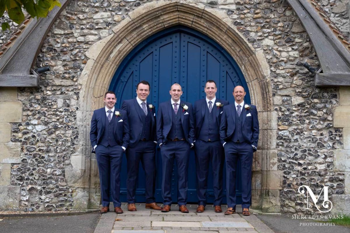 The groom and groomsmen pose in front of the church door